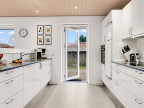 Une cuisine moderne avec des meubles blancs, une machine à café et une horloge au mur.
