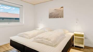 Un dormitorio con cama, mesita de noche, lámpara, ventana y un cuadro en la pared.