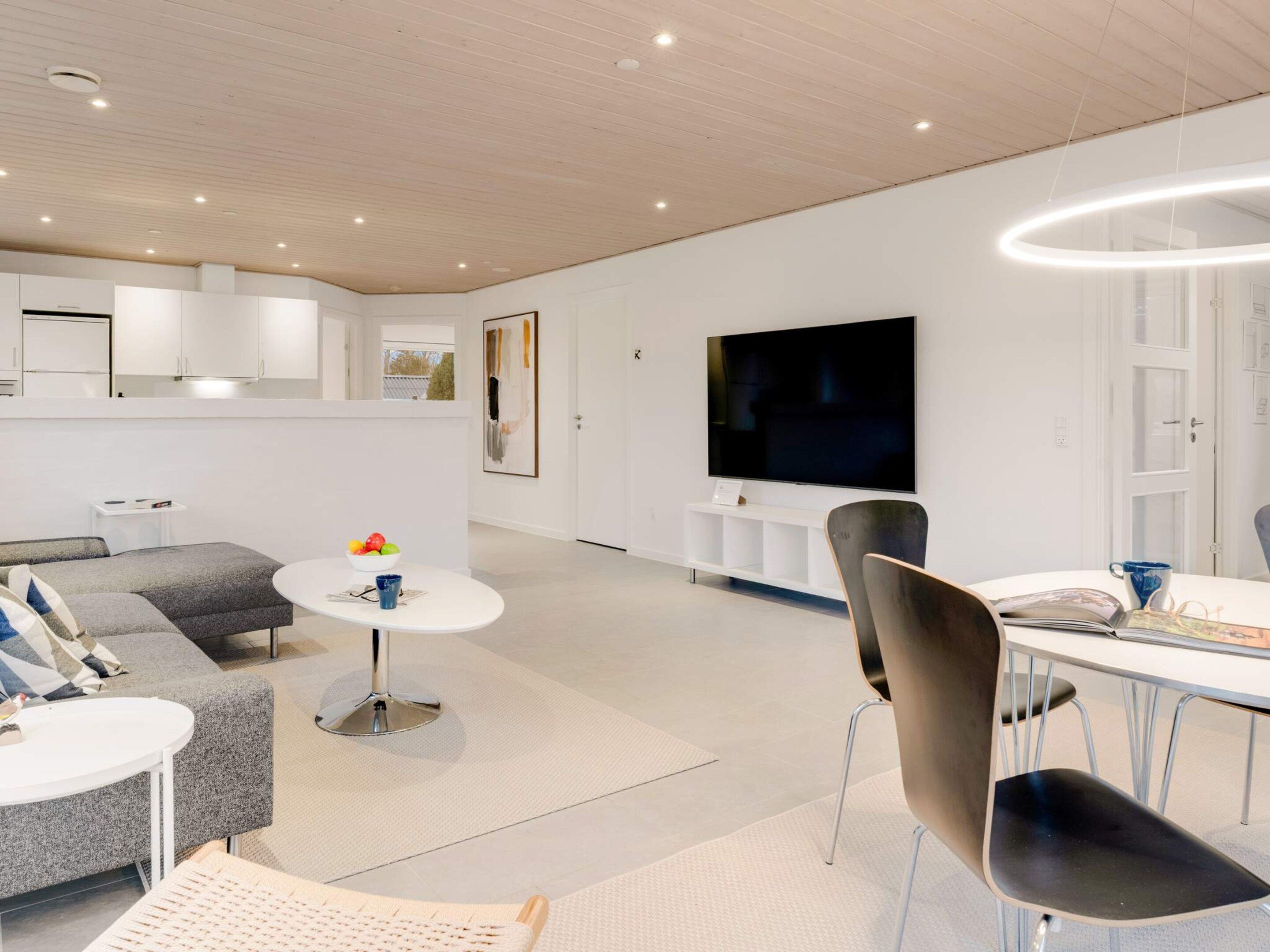 Una sala de estar moderna con sofá, mesa de comedor, sillas, televisor y área de cocina.