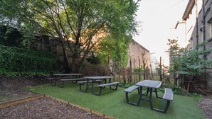 Un espace extérieur aménagé en terrasse, avec des tables de pique-nique et une surface herbeuse.