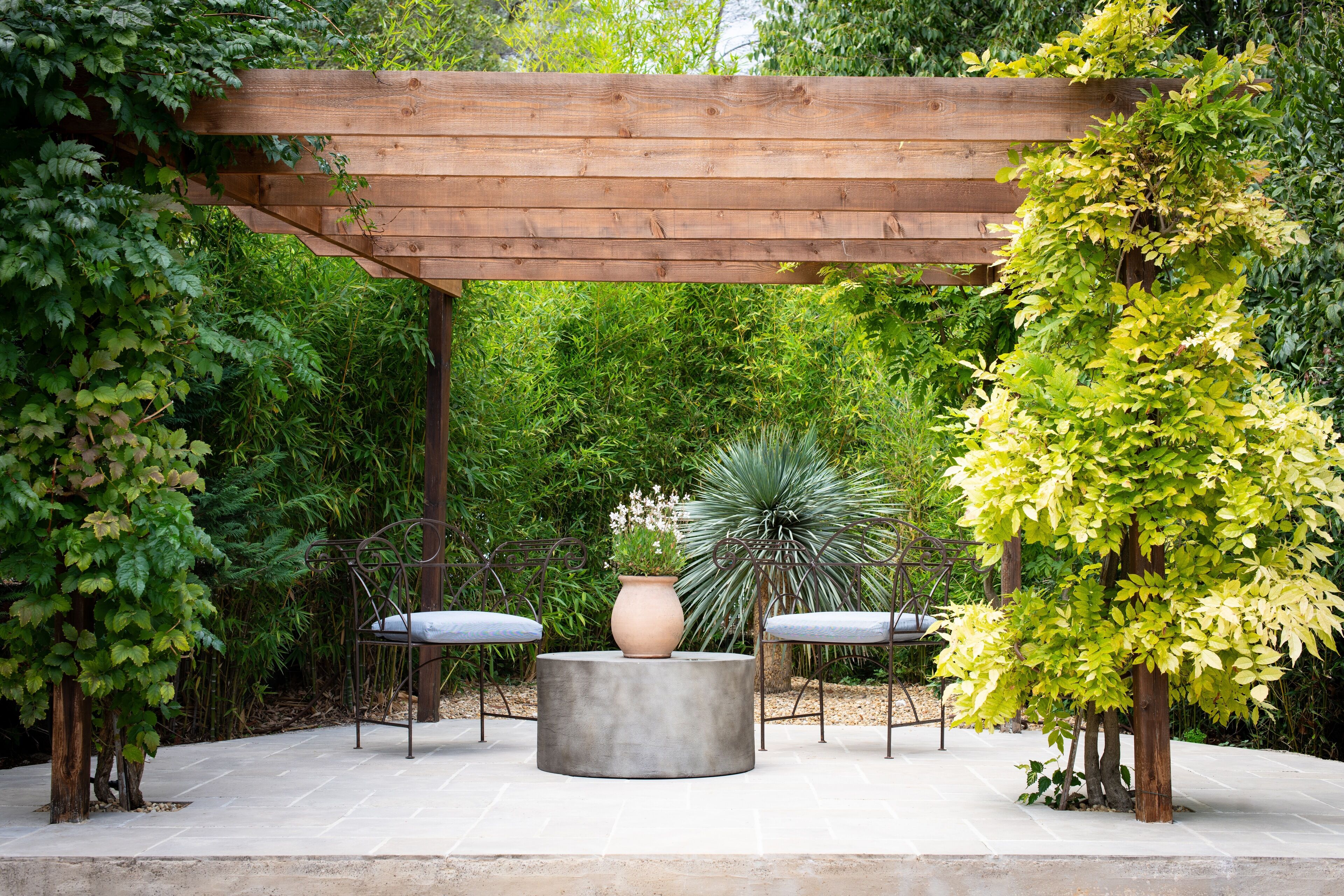 A wooden pergola with a round table and two chairs underneath.