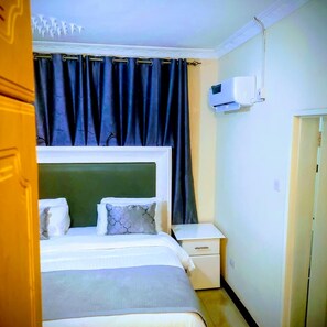 Un dormitorio con cama, mesita de noche, equipo de aire acondicionado y una puerta.