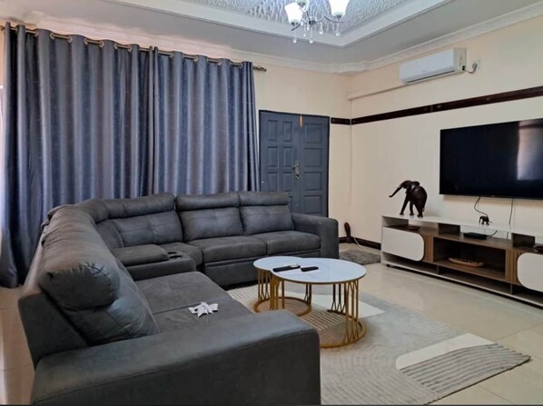 A living room with a sectional sofa, a round coffee table, a flat-screen TV, and a decorative elephant statue.