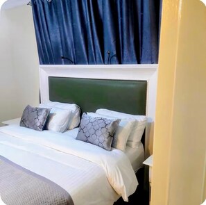 A bed with a white headboard, grey patterned pillows, and a blue curtain.