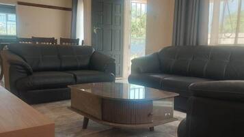 Een woonkamer met twee donkere banken, een houten salontafel en een eethoek met een tafel en stoelen.