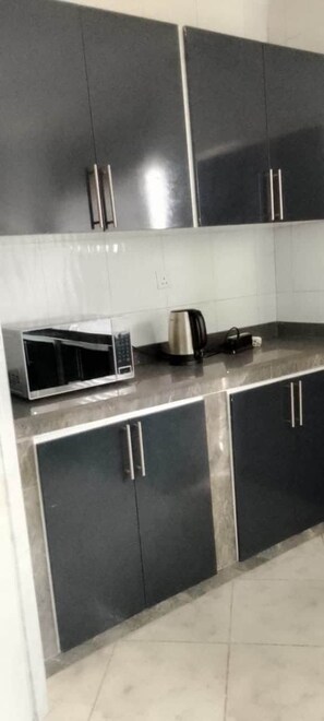 A kitchen with black cabinets, a microwave, a kettle, and a toaster.