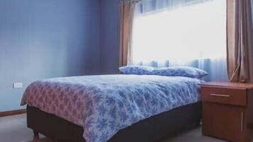 A bedroom with a bed, a nightstand, and a window with curtains.