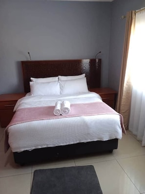 Una cama bien tendida con almohadas y una colcha, una mesita de noche y un cabecero.
