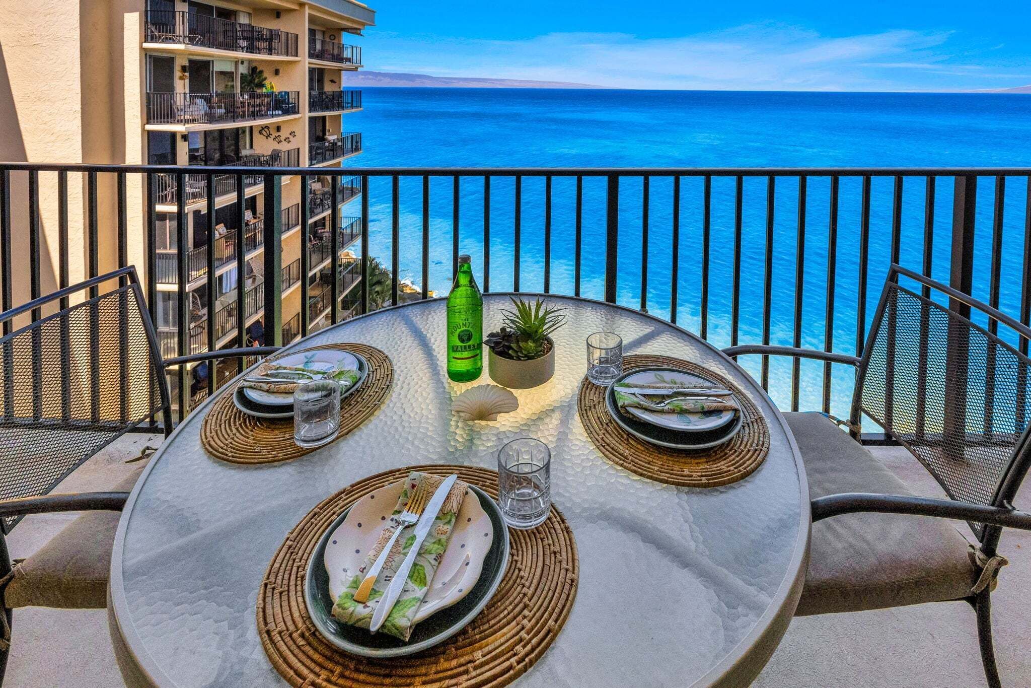 Mesa para cuatro con vista al océano, una botella de The Valley y una pequeña planta sobre la mesa.