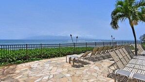 A stone patio with lounge chairs and a view of the ocean. - Island Style OceanFront 2BD Wonderful Views -Hololani A701 (Lahaina)