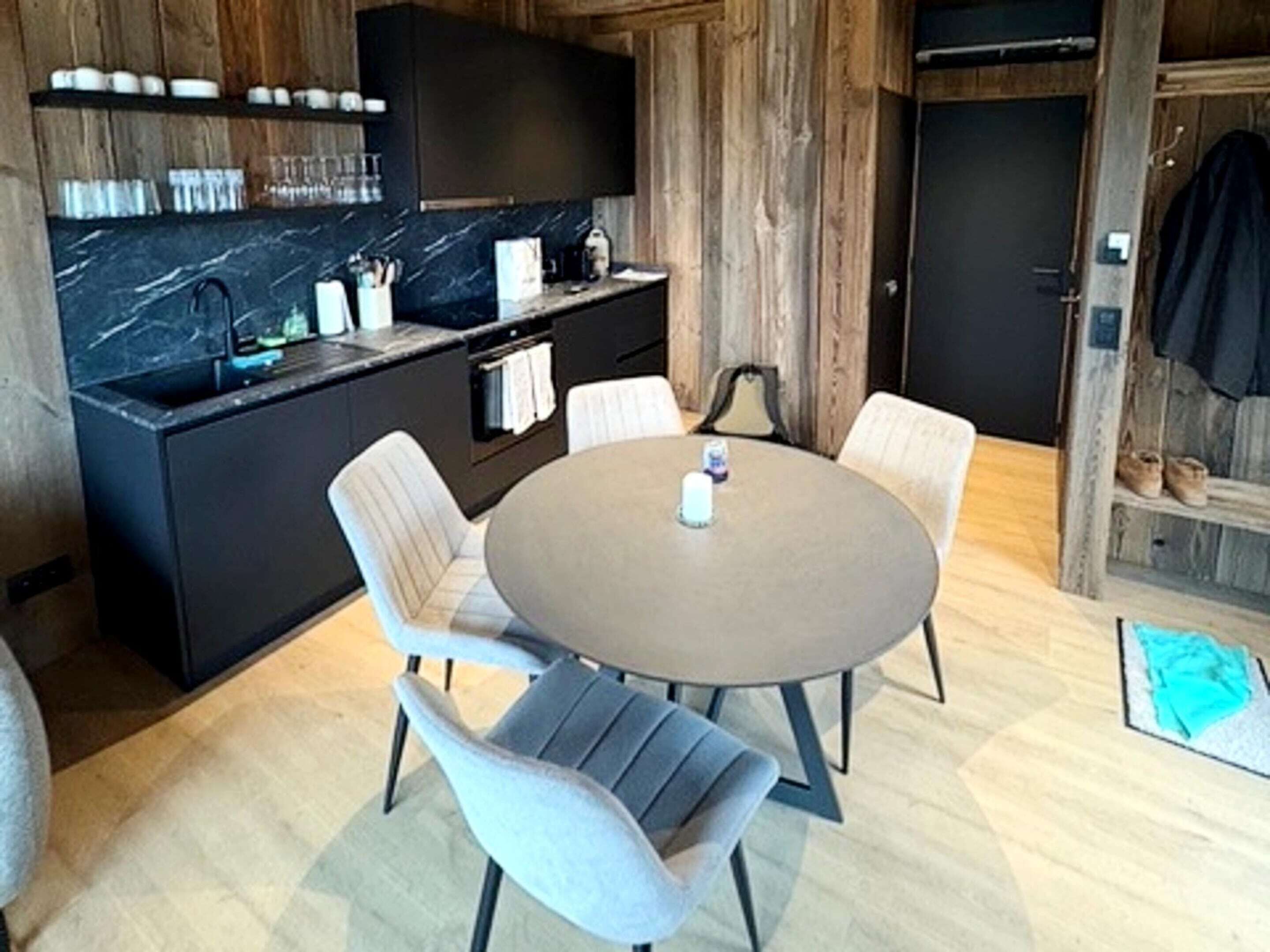 A modern kitchen with a marble countertop, a built-in oven, and a sink. There is a round table with four chairs in the dining area.