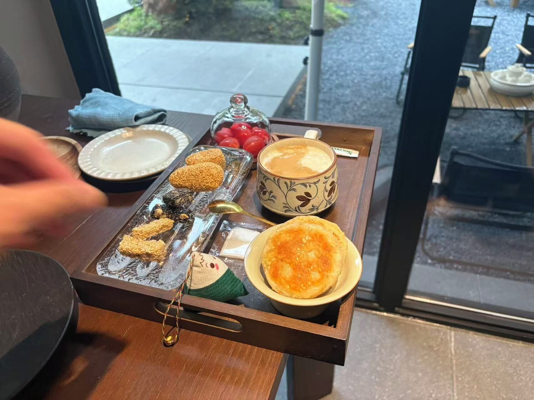 A tray with various food items and a cup of coffee on a wooden table near a window.