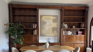 Un comedor con una mesa y sillas de madera, rodeado de estanterías y un cuadro abstracto de gran tamaño.