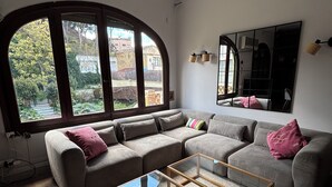Una sala de estar con un sofá modular, una mesa de centro de vidrio y un amplio ventanal con vistas al exterior.