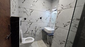 A bathroom with a toilet, bidet, and sink, all set in a marble-tiled room. - Hotel Pinaki (Ajmer)