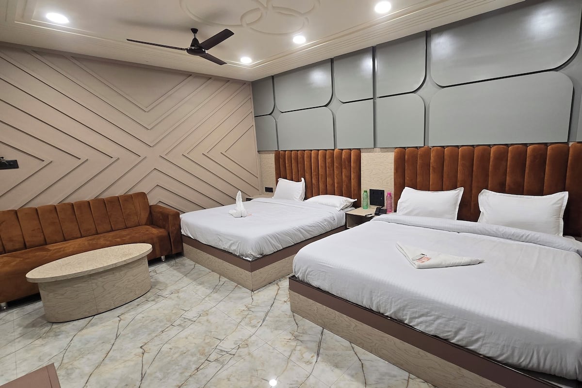 A hotel room with two beds, a sofa, a round table, and a ceiling fan.