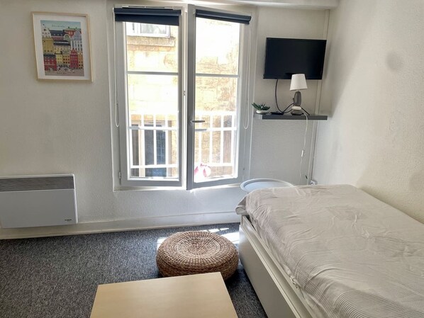 Une chambre à coucher avec un lit, une fenêtre, un téléviseur fixé au mur et une petite table.
