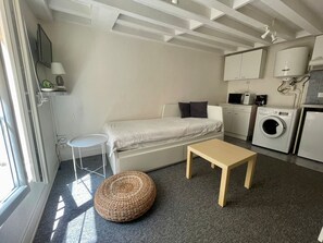 Un espacio habitable compacto con sofá, una mesita, un otoman redondo, lavadora y microondas.
