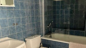 Ett badrum med blå kakelplattor, en vit toalett, ett vitt badkar och en korg av rotting.