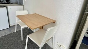Ett kompakt kök med ett litet kylskåp, en gasspis och ett handfat. Där finns ett träbord med två vita stolar.