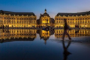 Ein historisches Gebäude mit einer zentralen Kuppel und symmetrischen Flügeln, umgeben von einer spiegelnden Wasseroberfläche.