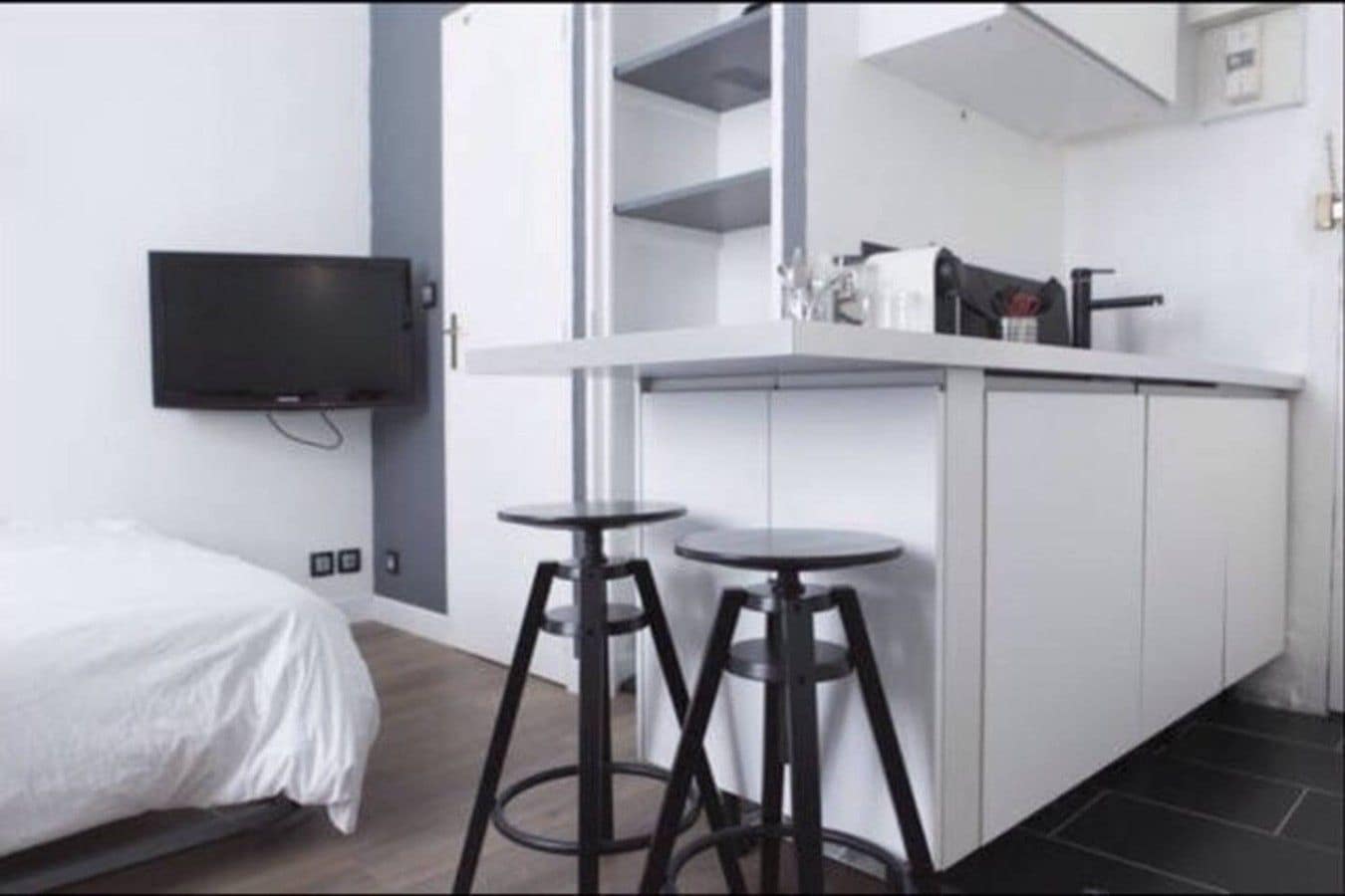Une chambre moderne équipée d’un lit, d’une télévision, d’une kitchenette avec réfrigérateur et de deux tabourets.