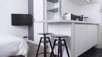 Une chambre moderne équipée d’un lit, d’une télévision, d’une kitchenette avec réfrigérateur et de deux tabourets.