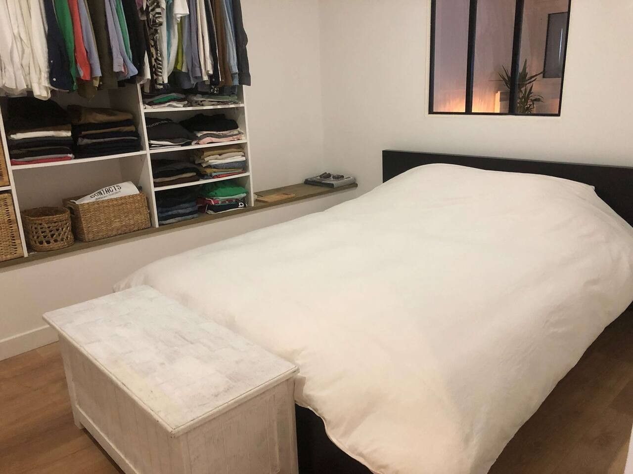 A neatly organized bedroom with a single bed, a bedside table, and a wardrobe with folded clothes.