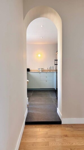 Ein Flur, der zu einer Küche mit modernem Design führt, mit Holzboden und einem weißen Bogen.