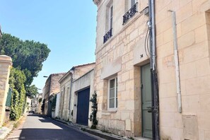 Une rue étroite bordée de bâtiments en pierre, dont certains sont dotés de portes et de fenêtres, et un ciel dégagé au-dessus.