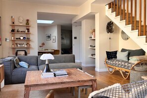 Un salon comprenant un canapé, une table basse, un fauteuil en osier et un escalier.