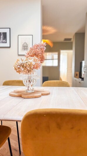 Une table à manger sur laquelle est posé un vase en verre transparent contenant des fleurs, lui-même placé sur un sous-verre en bois.