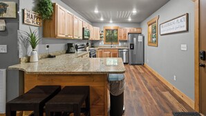 Una cocina con armarios de madera, encimeras de granito, refrigerador de acero inoxidable y una ventana con persianas.