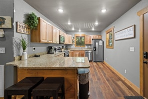 A kitchen with wooden cabinets, granite countertops, a stainless steel refrigerator, and a window with blinds. - The Ultimate Staycation: Indoor Pool, Hot Tub & Game Room Cabin (Sevierville)