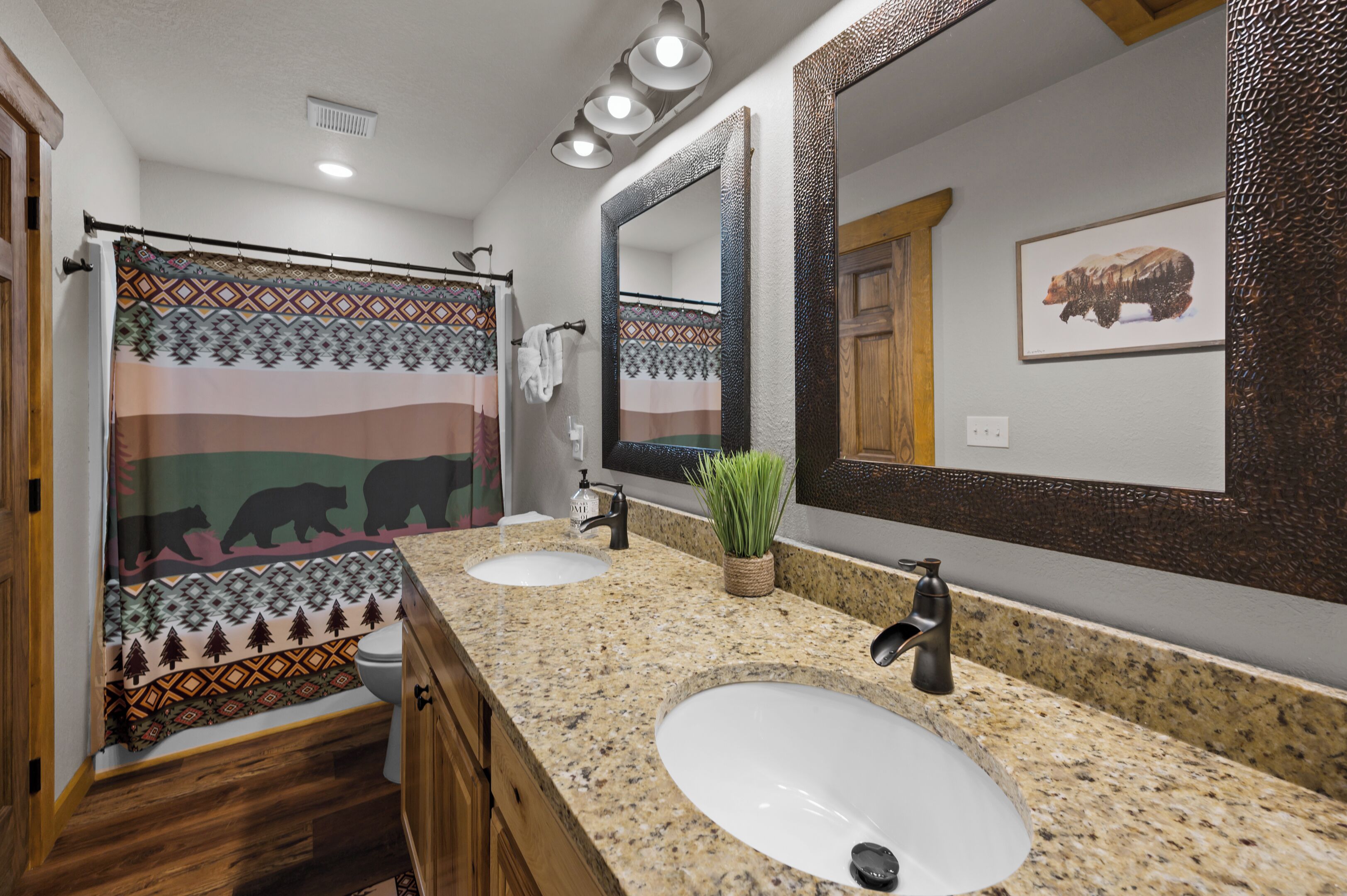 A bathroom with two sinks, a large mirror, a shower curtain with a bear design, and a wooden door.