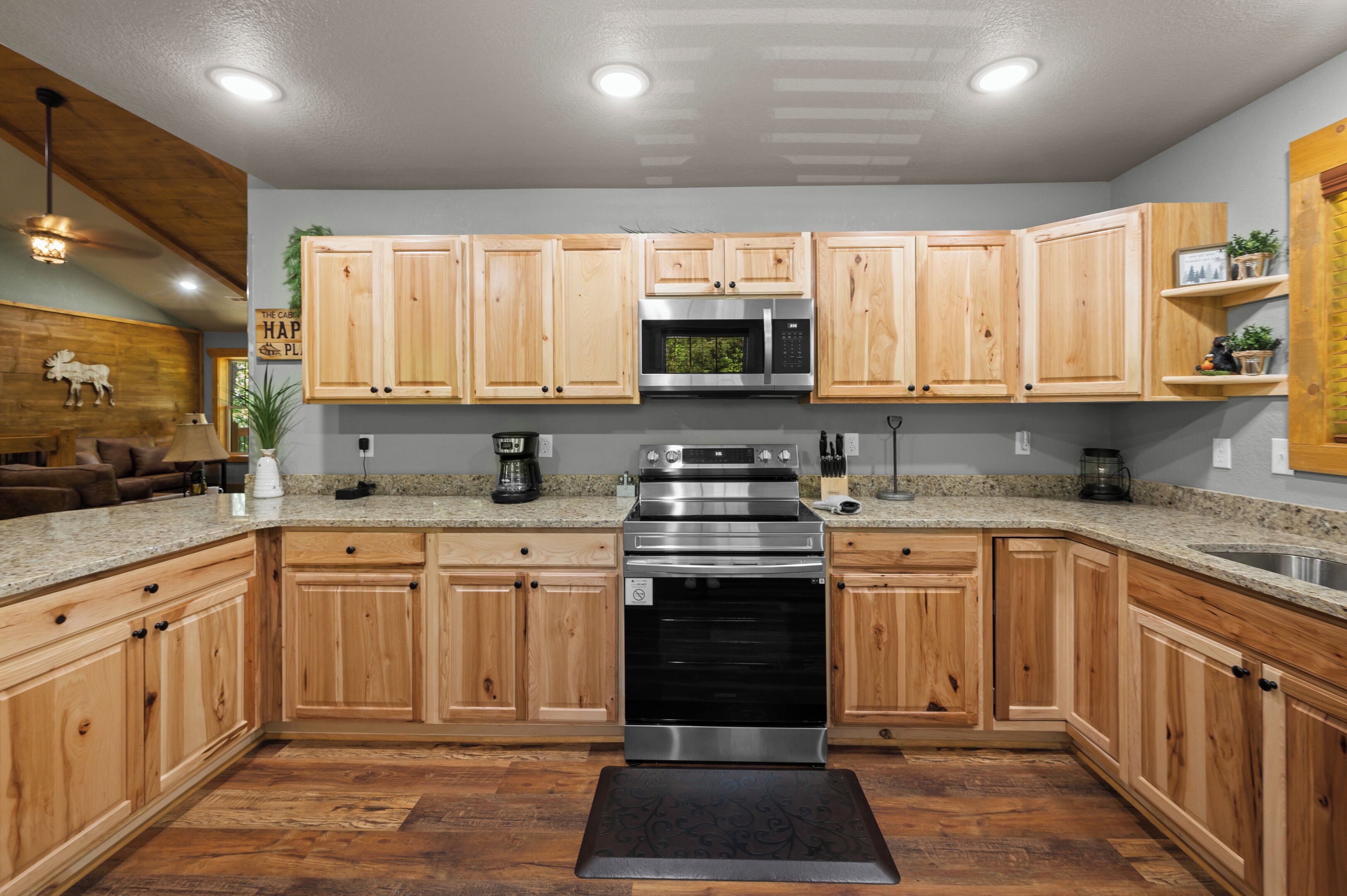 A kitchen with wooden cabinets, stainless steel appliances, granite countertops, and a black rug.