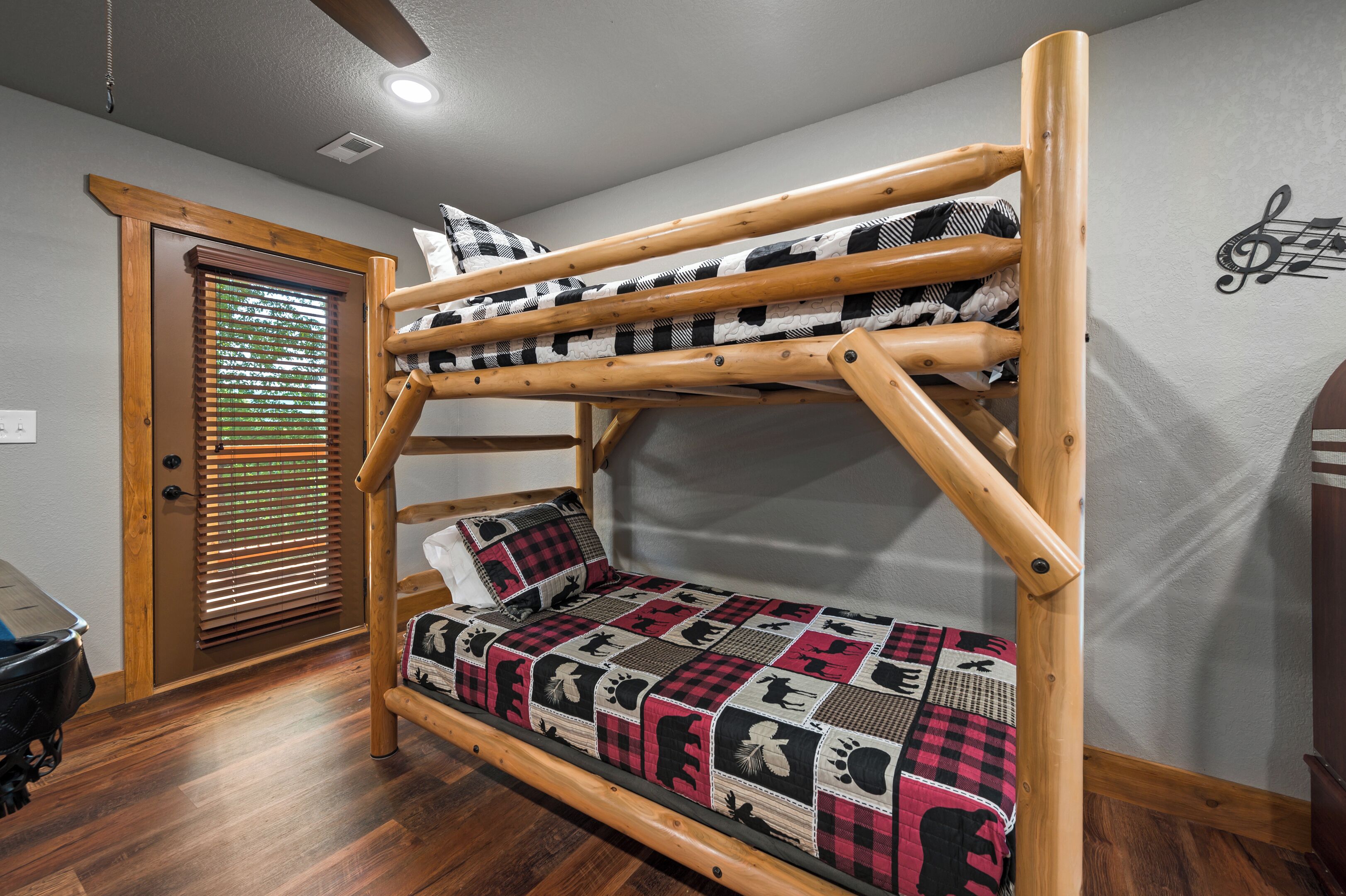 A bunk bed with a checkered blanket, a wooden door with blinds, and a wall with a musical note design.