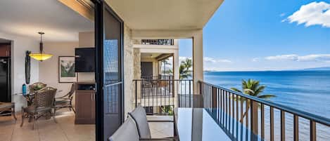 A balcony with a glass table and chairs overlooking the ocean.