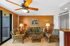 Ein Wohnzimmer mit Deckenventilator, einer Couch, zwei Sesseln, einem Couchtisch und zwei Lampen.