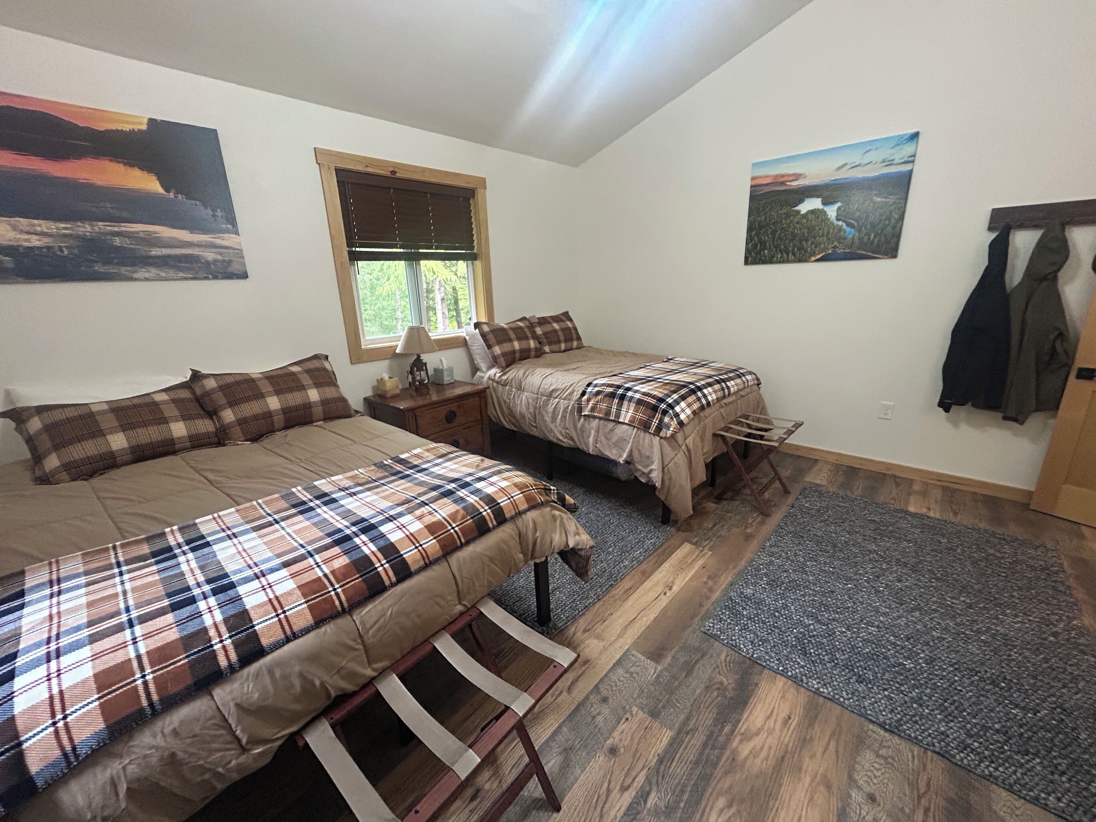 Une chambre avec deux lits, une fenêtre, une table de chevet et un porte-manteau.
