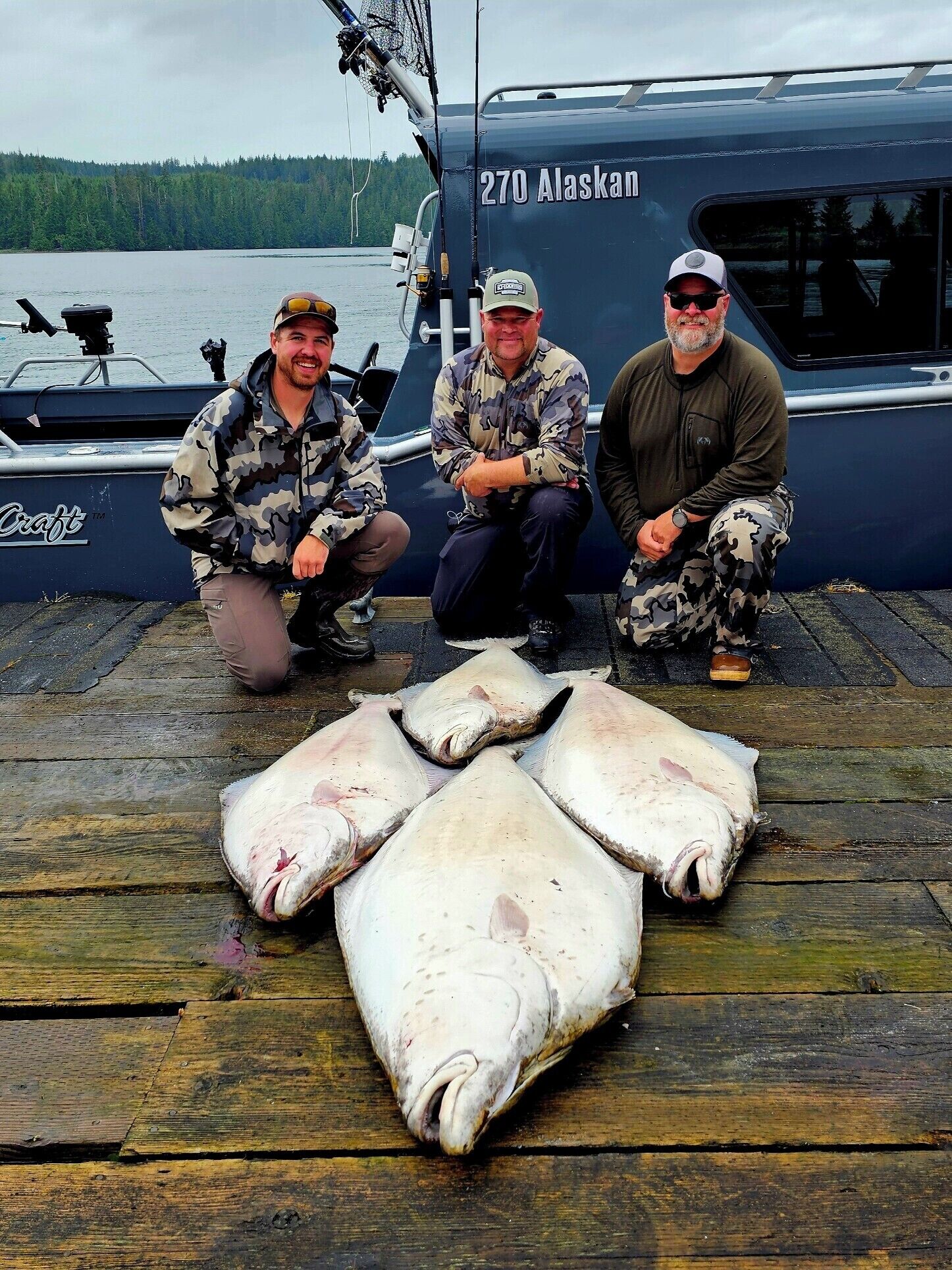 Three people on a boat deck with large fish laid out in front.