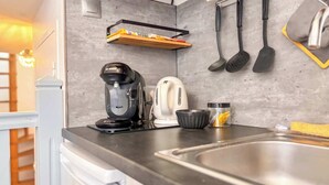 Ett kök med en kaffebryggare från Bosch, en vit vattenkokare, en diskho i rostfritt stål och köksredskap som hänger på väggen.