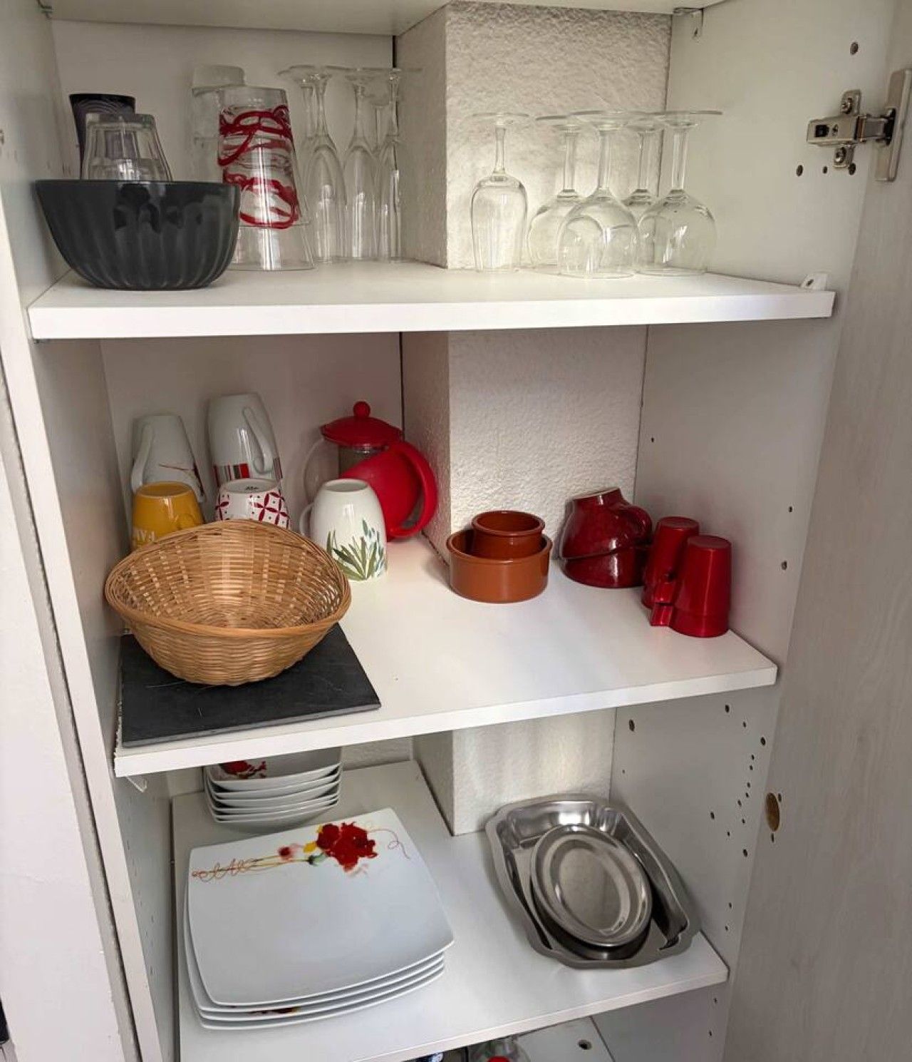 A kitchen with shelves containing glassware, a basket, and various kitchen utensils.