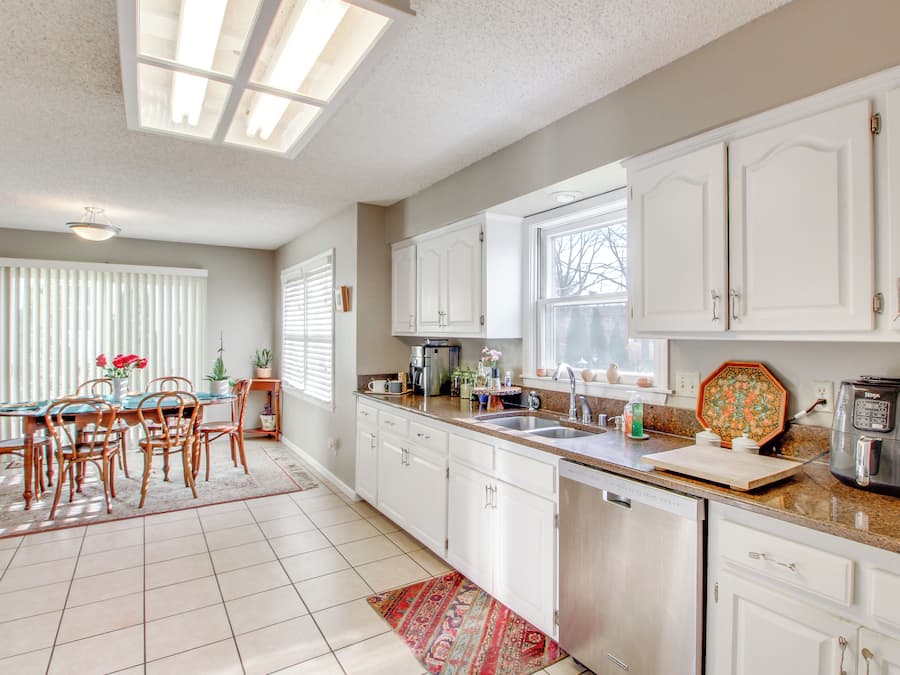 A kitchen with white cabinets, a dining table with chairs, a coffee maker, and a dishwasher.