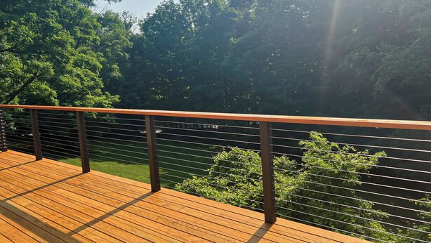Una terraza de madera con barandilla metálica que da a un paisaje verde exuberante.