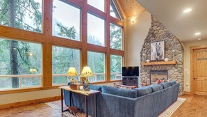 A spacious living room with a large window, a stone fireplace, and a cozy seating area. - 'white Water Lodge' Luxe Leavenworth Vacation Home (Leavenworth)