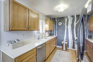 Una cocina con armarios de madera, un lavamanos de acero inoxidable y una pared con un mural de un árbol.