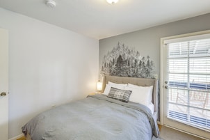 Un dormitorio con cama, cabecera, lámpara de pared y puerta con persianas.
