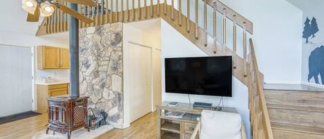 Un salon moderne avec un escalier en bois, un mur en pierre, une cheminée et un téléviseur à écran plat.