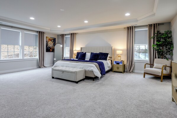 A spacious bedroom with a large bed, a sitting area, and a view of the city. - 1 Mile to Quantico: 5BR Home w/ Game Room! (Triangle)